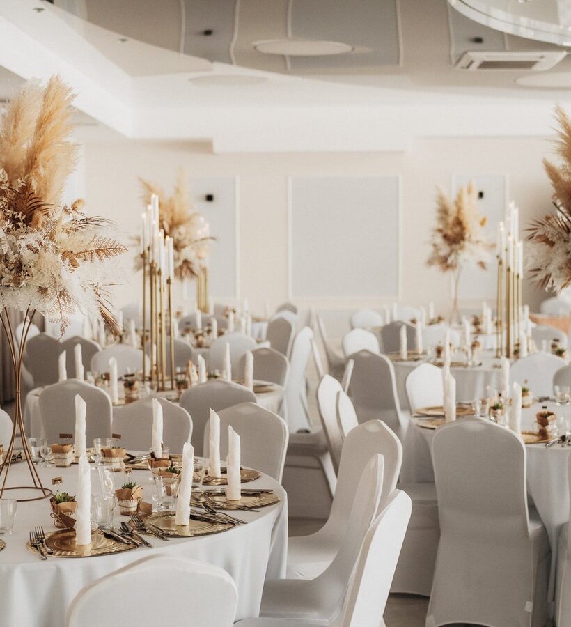Elegant banquet hall with round tables adorned with white linens, gold accents, and dried floral centerpieces.