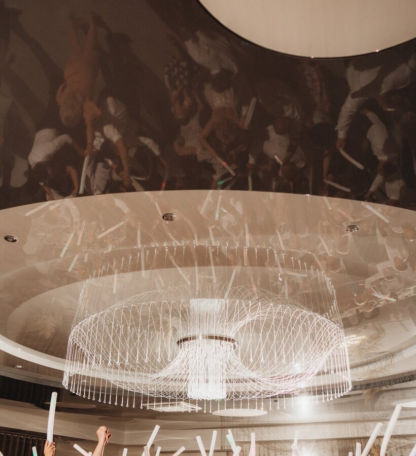 Luxury ballroom with a modern, intricate chandelier and guests enjoying celebration with glowing light sticks.