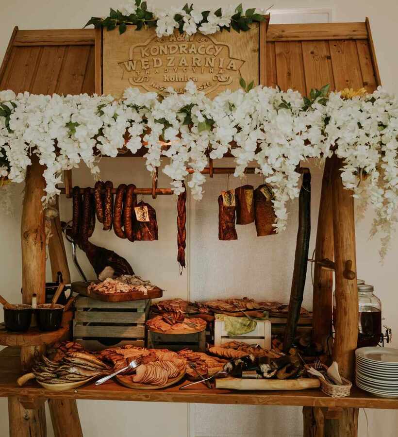 Rustic wooden table with assorted smoked meats, sausages, and fish on a buffet decorated with white flowers