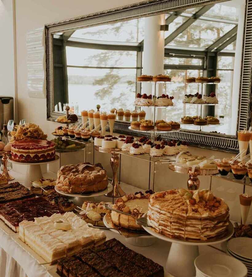 Dessert buffet showcasing assorted cakes, tarts, and parfaits in a bright, elegant room with a large decorative mirror