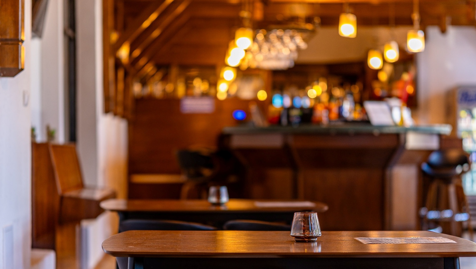 Przytulny bar hotelowy z drewnianym wnętrzem, zawieszonymi lampami i szklanym świecznikiem na stoliku