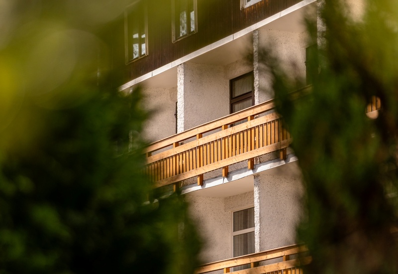 Balkonowy pokój w górskim pensjonacie z drewnianymi balustradami, widok przez zieleń, spokojna atmosfera.