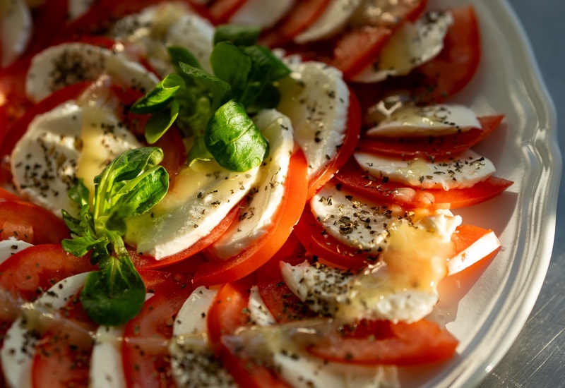 Talerz sałatki Caprese: naprzemienne plasterki pomidora i mozzarelli, skropione oliwą, posypane ziołami, z bazylią.