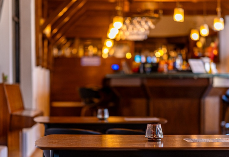 Przytulny bar hotelowy z drewnianym wnętrzem, zawieszonymi lampami i szklanym świecznikiem na stoliku