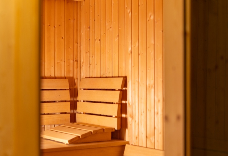 Drewniana sauna z podwójnymi ławkami, odchylanymi oparciami i ciepłym oświetleniem — relaks w strefie spa hotelu.