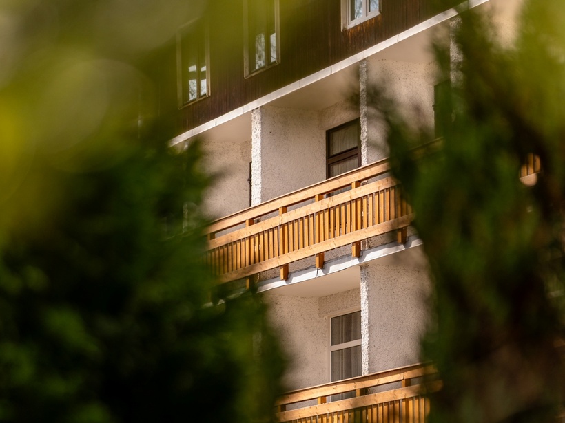 Balkonowy pokój w górskim pensjonacie z drewnianymi balustradami, widok przez zieleń, spokojna atmosfera.