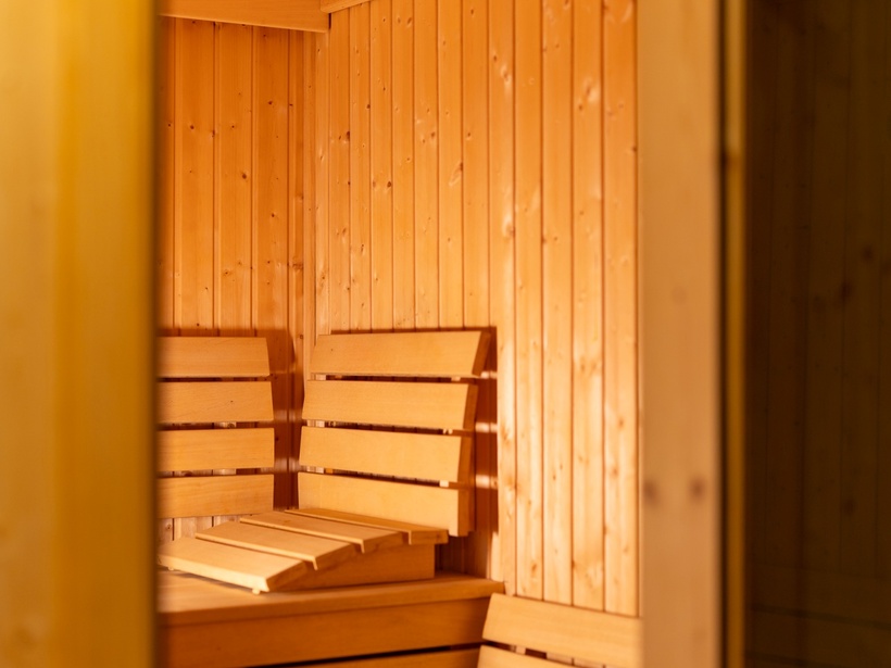 Drewniana sauna z podwójnymi ławkami, odchylanymi oparciami i ciepłym oświetleniem — relaks w strefie spa hotelu.