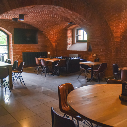 Gemütliches Restaurant im gewölbten Ziegelkeller mit Bogenfenstern, Holztischen, Ledersofas und warmem Licht