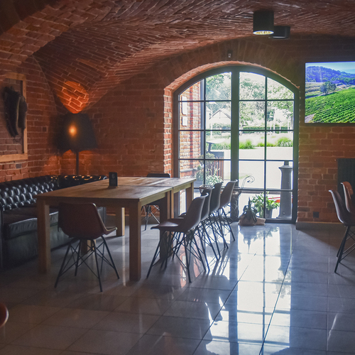 Hotel-Lounge mit Ziegelgewölbe, Bogenfenster, gemeinsamer Holztisch, Ledercouch, stimmungsvoller Beleuchtung und Wand-TV