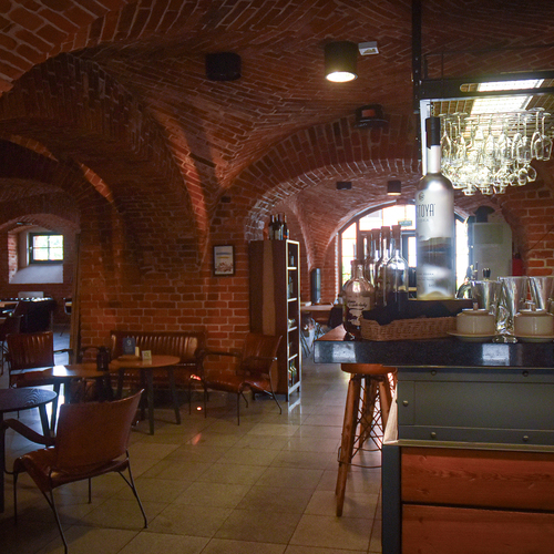 Gemütliche Hotelbar im Keller mit roten Backsteinbögen, Lederstühlen, Flaschen und hängenden Weingläsern an der Theke.
