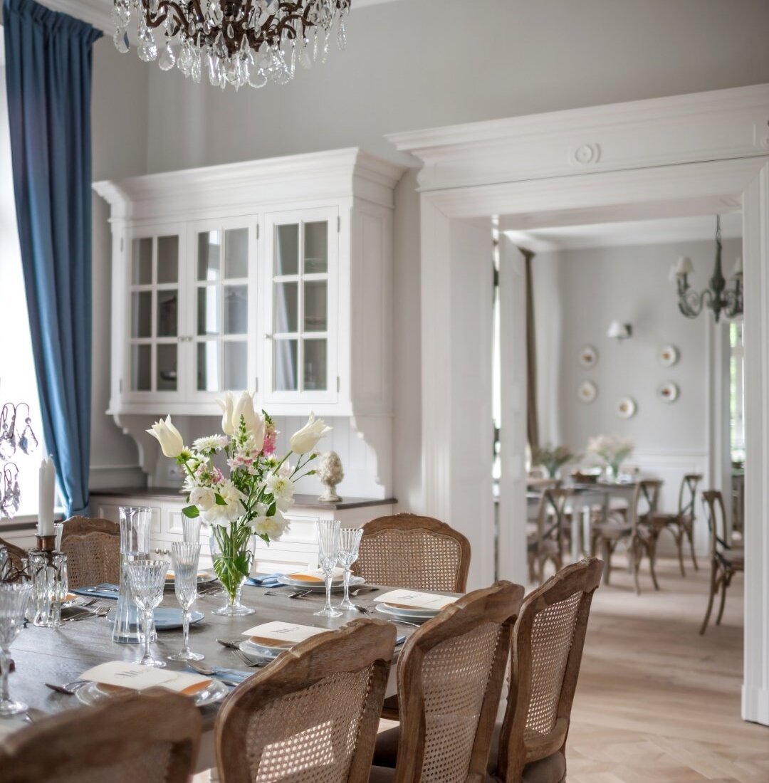 Sala kredensowa w Pałacu Kamieniec. Duży stół rodzinny. Białe kredensy oraz kryształowe żyrandole