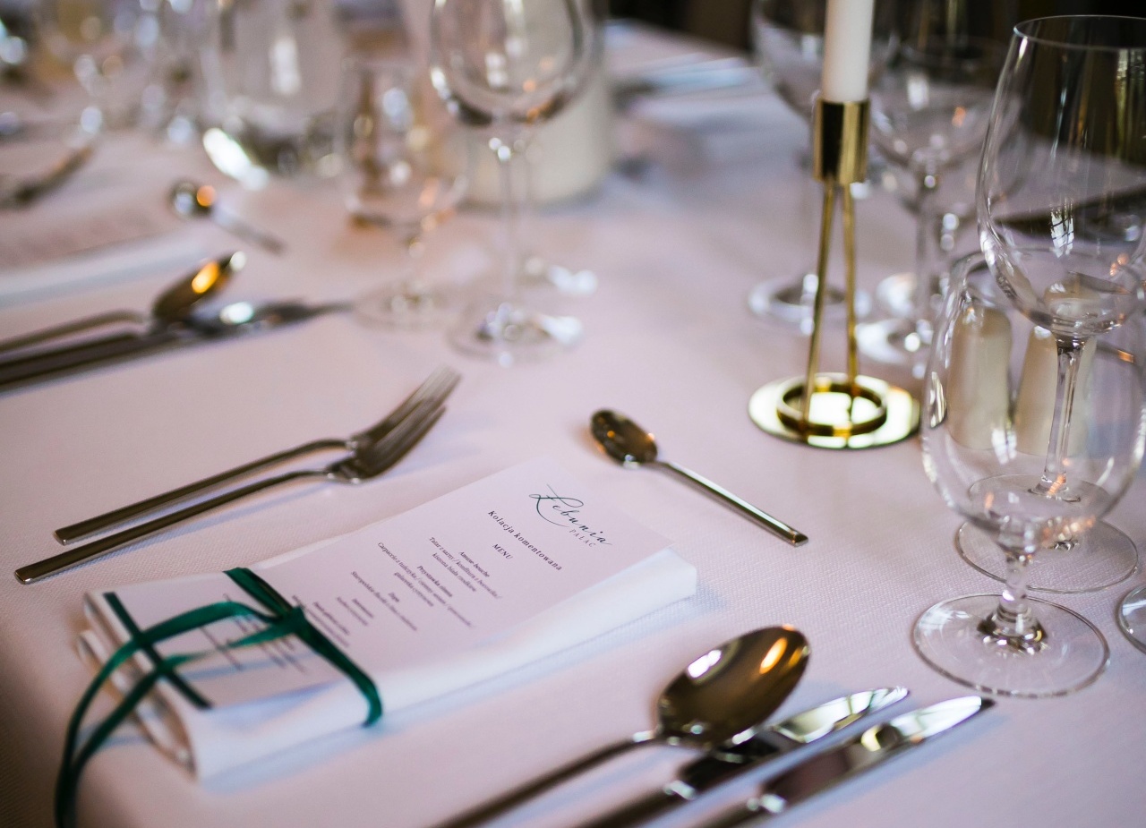 Elegancka zastawa na białym obrusie z menu przewiązanym zieloną wstążką, błyszczącymi sztućcami, kieliszkami i świecą.
