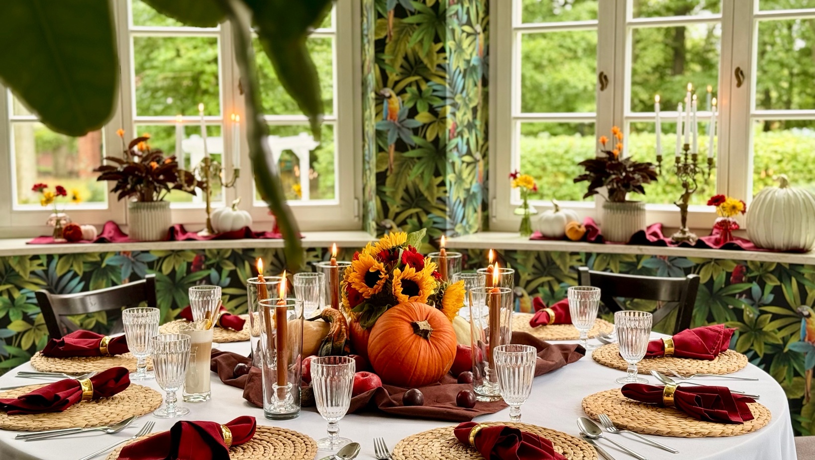 Okrągły stół nakryty na jesienny posiłek z dynią i słonecznikami, palącymi świecami, kryształowymi kieliszkami i widokiem na ogród