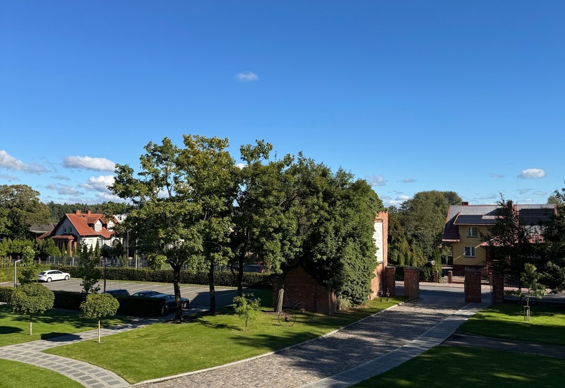 Zadbane dziedzińce z krzyżującymi się brukowanymi alejkami, zielonym trawnikiem, drzewami i ceglanym wejściem.