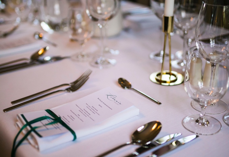 Elegancka zastawa na białym obrusie z menu przewiązanym zieloną wstążką, błyszczącymi sztućcami, kieliszkami i świecą.
