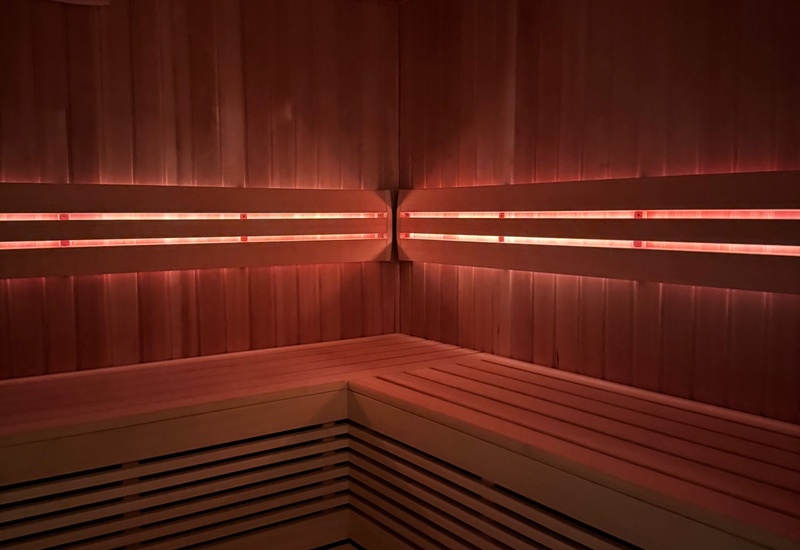 Sauna spa z drewnianymi, narożnymi, piętrowymi ławkami, ciepłym czerwonym podświetleniem LED i widocznym termometrem oraz higrometrem