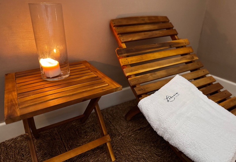 Drewniany leżak z złożonym haftowanym białym ręcznikiem, obok świeca w szklanym naczyniu na stoliku, atmosfera SPA