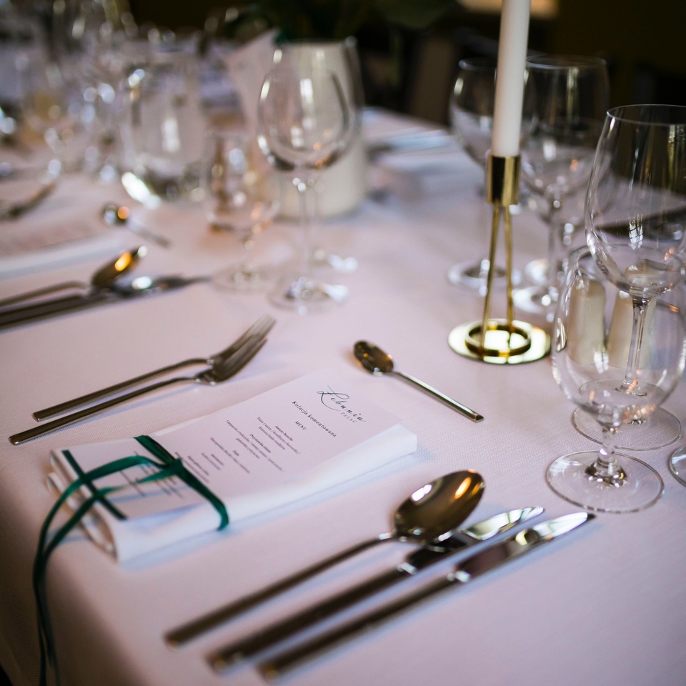 Elegancka zastawa na białym obrusie z menu przewiązanym zieloną wstążką, błyszczącymi sztućcami, kieliszkami i świecą.