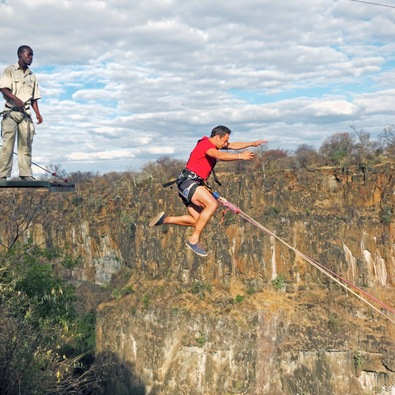 Person mit Gurt springt von Plattform in Schlucht beim Bungee-Sprung, begleitet von Betreuer