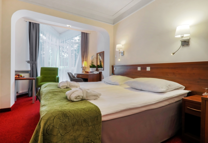 Duże łóżko w pokoju Standard Plus z wygodnym fotelem, biurkiem i dużym oknem