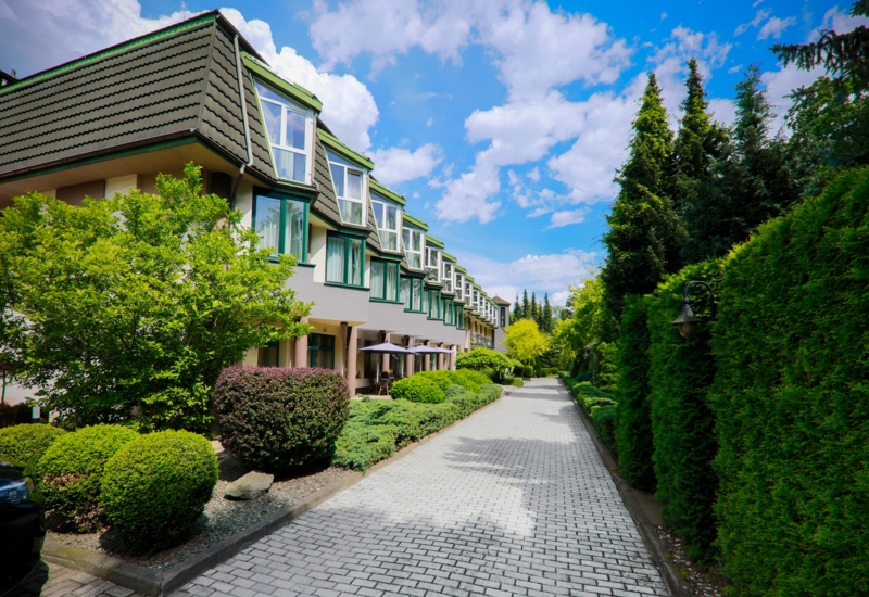 Spacerowa alejka wokół hotelu otoczona zielenią i widokiem na obiekt