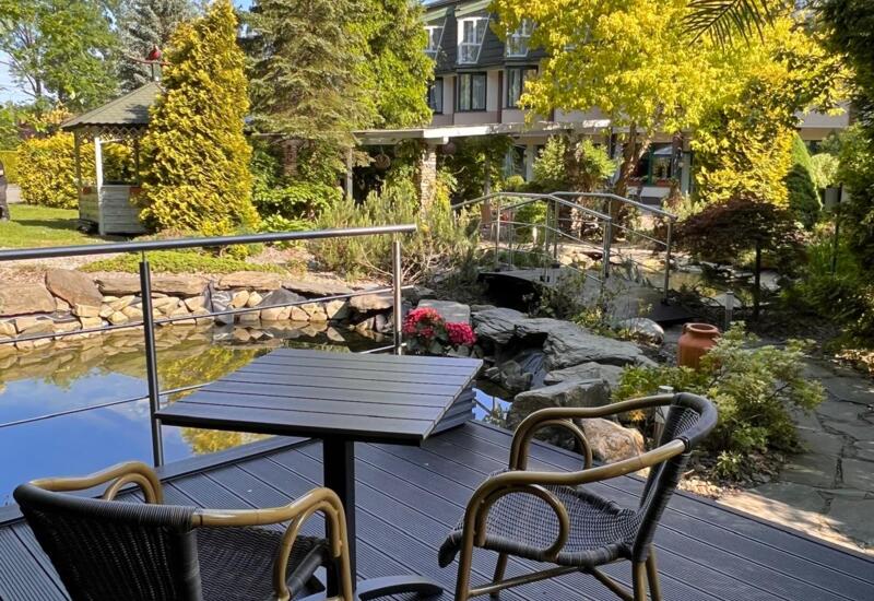 Stolik z krzesłami na tarasie hotelowym z widokiem na ogród i oczko wodne