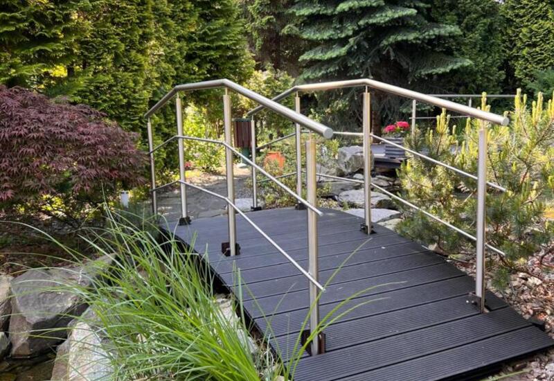 Drewniana kładka nad wodą w otoczeniu zieleni w ogrodzie hotelu Papuga Park