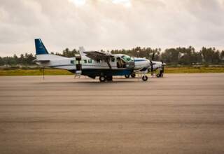 Small twin-engine propeller plane parked on tarmac at tropical airport with palm trees and cloudy sky in the background