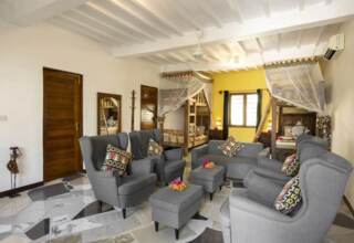 Bright, cozy shared room with twin wooden bunk beds draped with mosquito nets, modern gray seating, patterned pillows, and tiled floors.