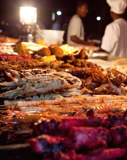 Variety of grilled seafood and meat skewers displayed on a night market stall with chefs preparing food in the background