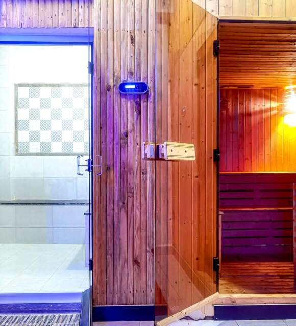 Modern wooden sauna room with warm lighting and adjacent tiled steam room door in a spa facility