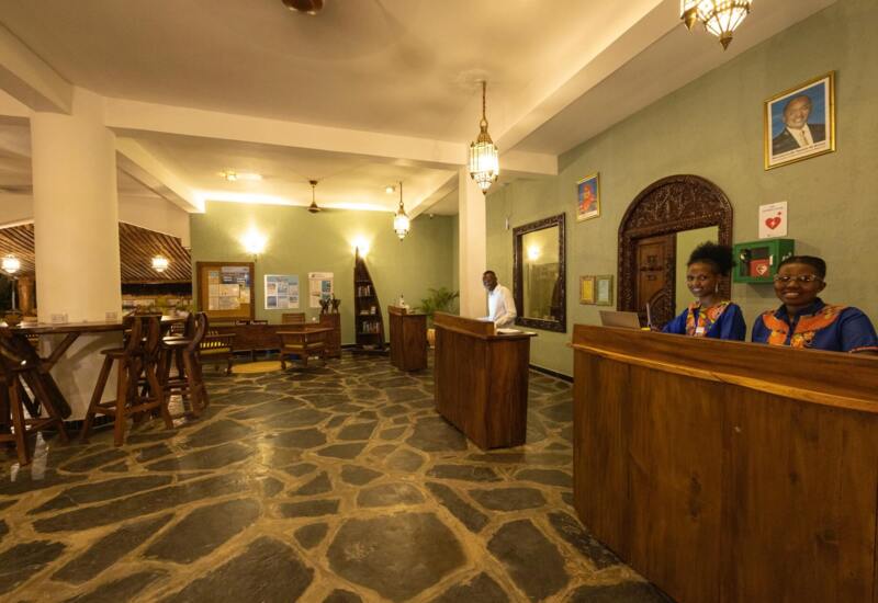Hotel reception area with warm lighting, stone flooring, wooden desks attended by smiling staff in colorful uniforms, and traditional decor.