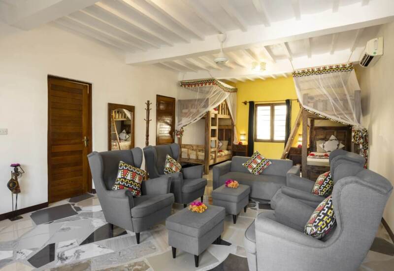 Bright, cozy shared room with twin wooden bunk beds draped with mosquito nets, modern gray seating, patterned pillows, and tiled floors.