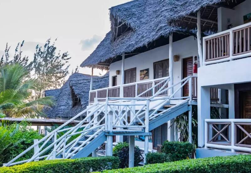 Tropical hotel with white wooden balconies, thatched roofs, surrounded by lush greenery and palm trees at sunset