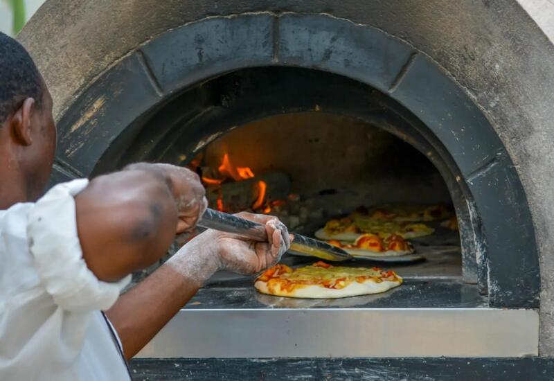 Chef placing fresh pizza into a traditional wood-fired stone oven with glowing flames, highlighting authentic cooking