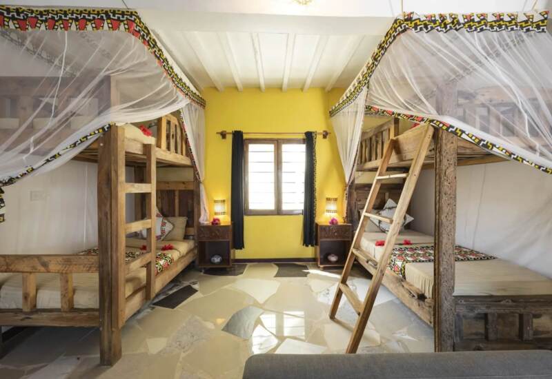 Bright room with twin wooden bunk beds topped with mosquito nets, colorful decorative trim, and bedside tables with lamps