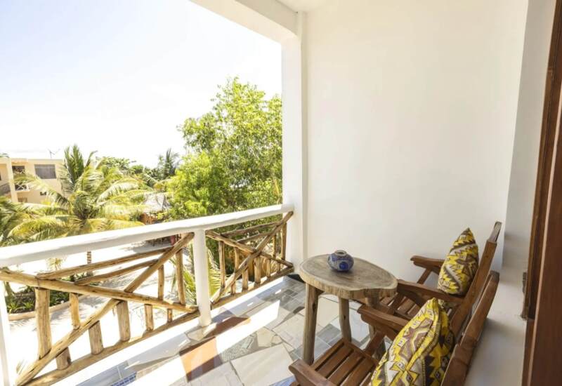 Cozy balcony with rustic wooden railing and chairs featuring patterned yellow cushions, overlooking lush tropical greenery.