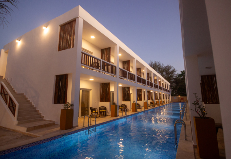 Modern two-story hotel with private patios overlooking a long illuminated outdoor pool at dusk