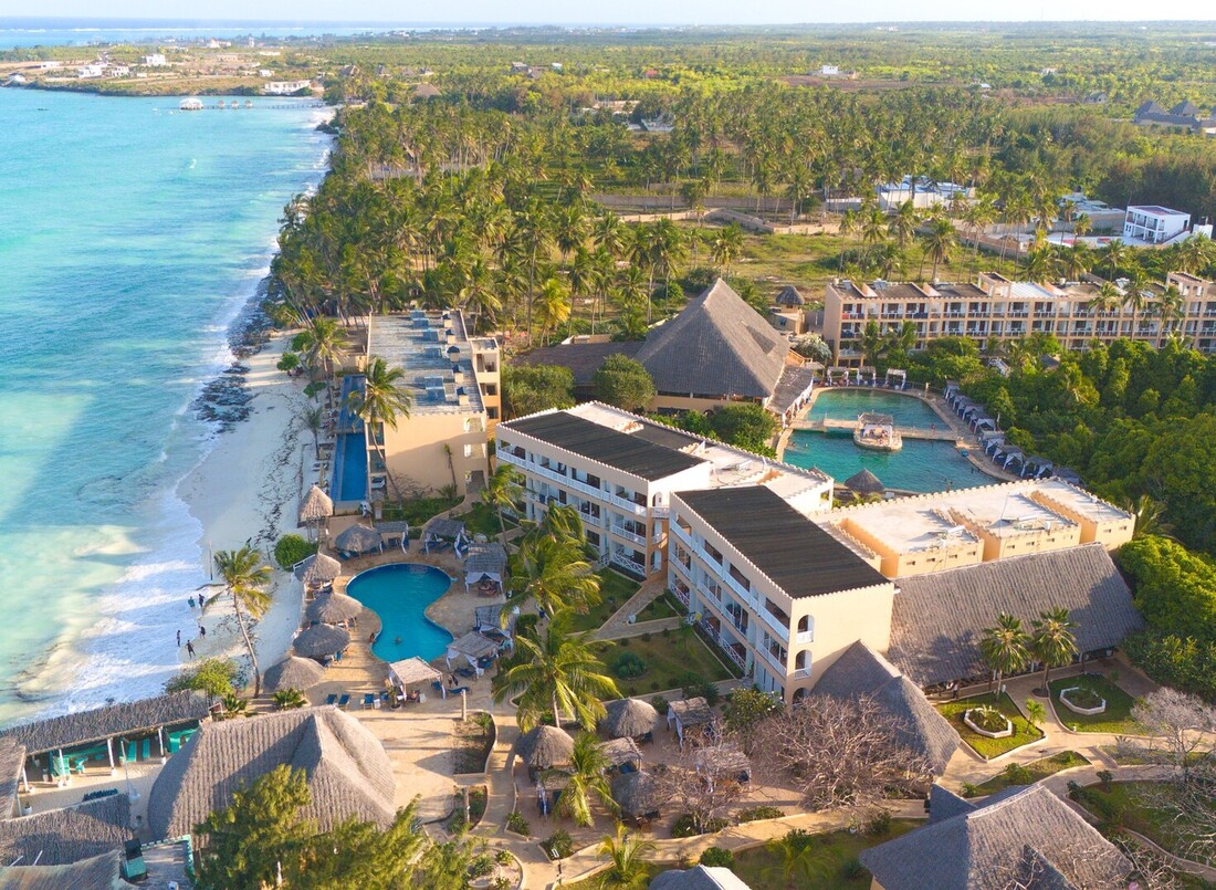 Beachfront resort with turquoise sea and white sand, palm-lined grounds, thatched-roof pavilions, pools and balcony rooms.