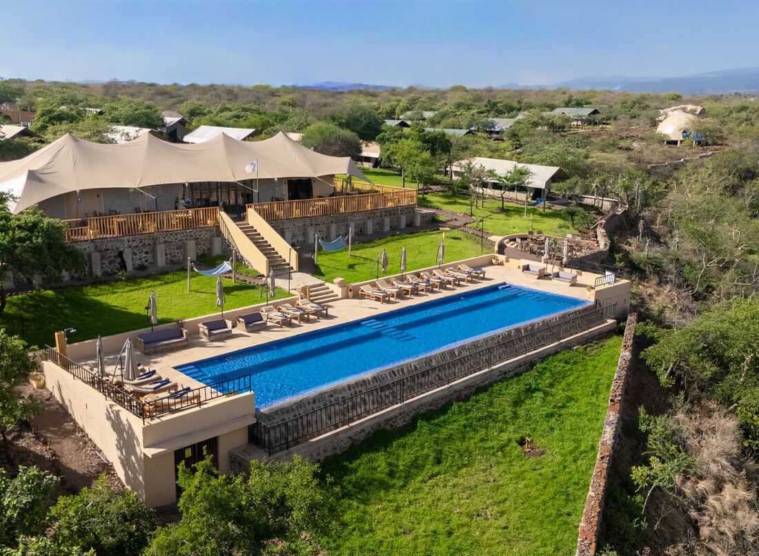 Tented safari lodge with long rectangular pool and sun loungers on a raised stone terrace, hammocks and bushland views