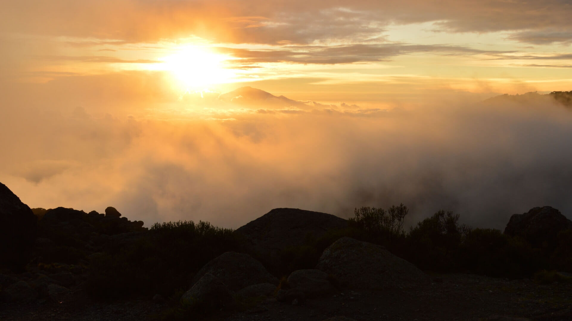 Golden sunrise illuminating misty mountain landscape with rocky terrain and soft clouds creating a tranquil outdoor view
