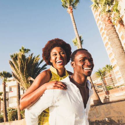 Happy couple enjoying a sunny day near a beachfront hotel with tall palm trees and clear blue sky