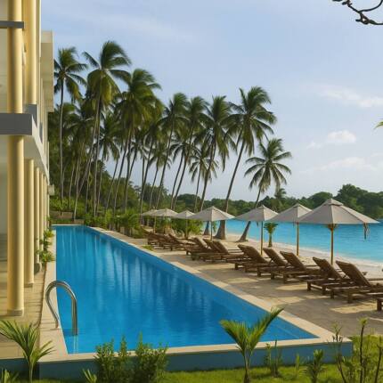 Beachfront hotel pool with lounge chairs and umbrellas by sandy shore, palm trees, and a calm ocean view under clear sky