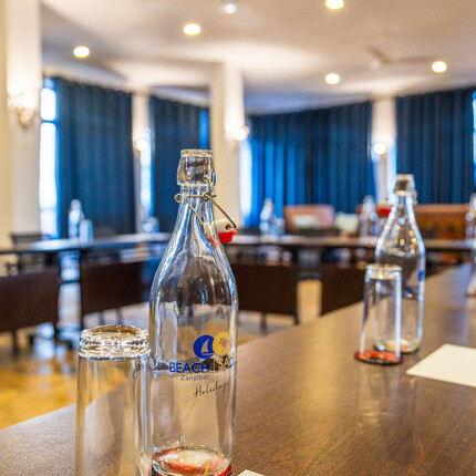 Meeting room with long wooden table, branded Beach Safari water bottles, glasses and notepads, dark blue curtains and warm lighting