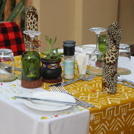 Table set with mustard-patterned runner, leopard-print napkins, wine glasses, green candle, small succulent in beaded pot and cutlery