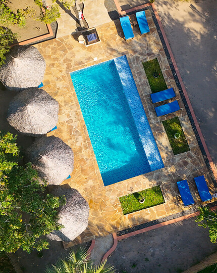 Secluded hotel swimming pool on stone terrace with blue loungers and thatched umbrellas tucked into lush tropical greenery.