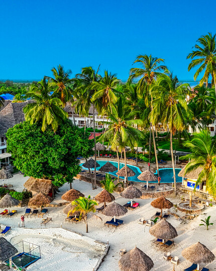 Tropical beachfront resort with white-sand beach, palm-shaded palapas, sun loungers, thatched villas and lagoon pool.