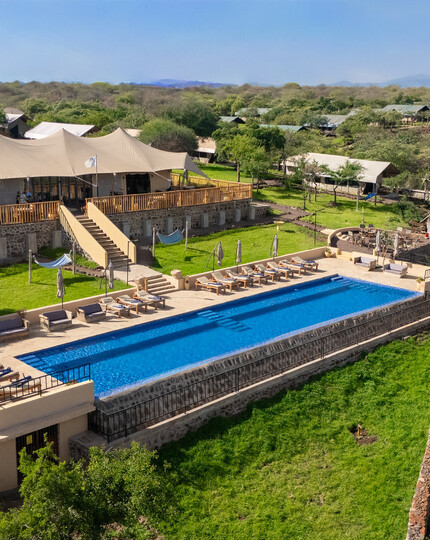 Safari lodge with canvas main tent, elevated deck and long blue pool with sunbeds, hammocks and sweeping savannah views.
