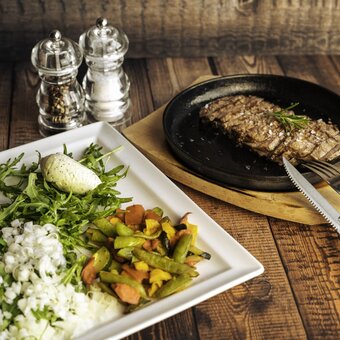 Sliced grilled steak in a cast-iron skillet with rosemary and sea salt, served with roasted potatoes and arugula salad.