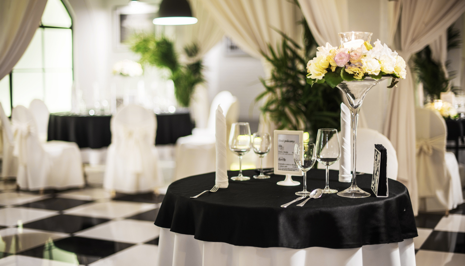 Elegantně prostřený stůl v hotelové restauraci s černým ubrusem, bílými židlemi a květinovou dekorací.